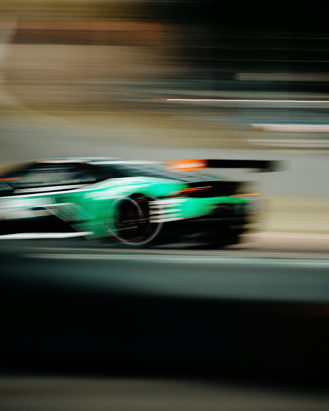 A green racing car speeds along a dark track.