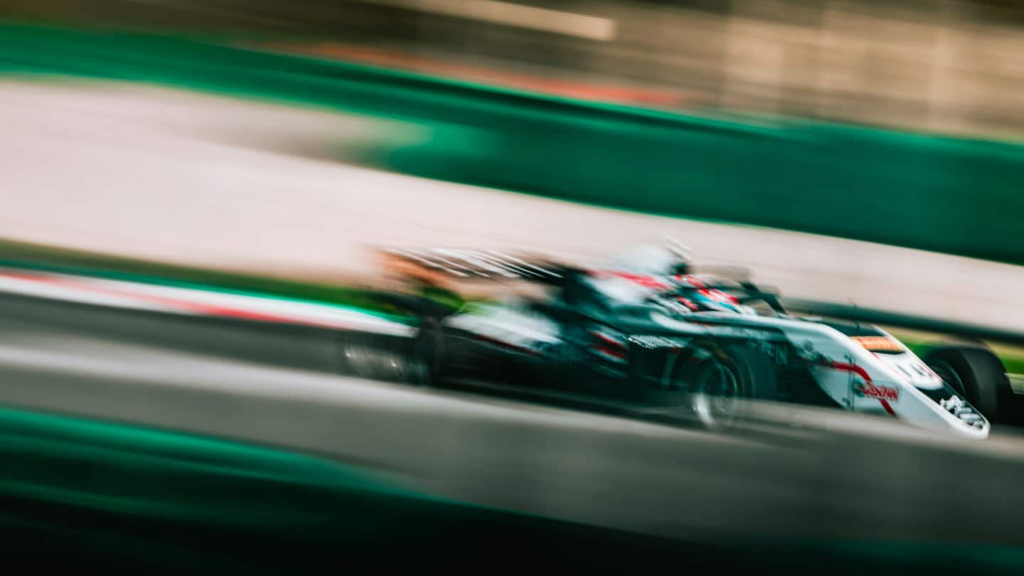 A race car speeds along a track near green barriers.