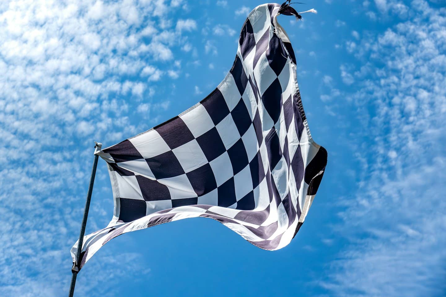 A black and white checkered flag waves against a blue sky.