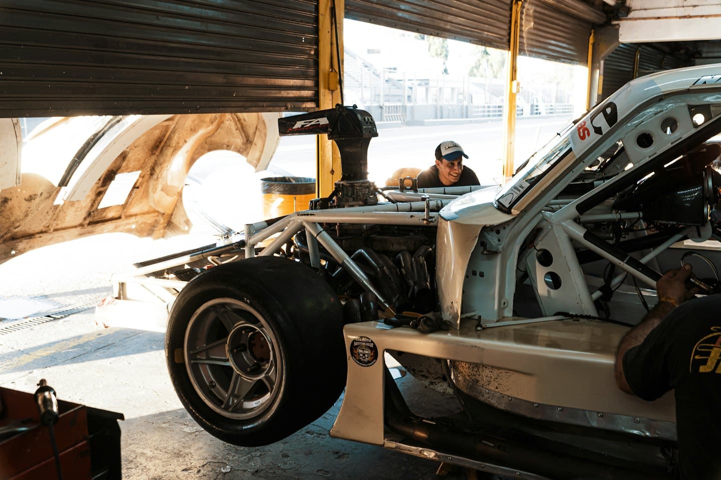 Mechanics working on a race car in a garage with a racetrack outside.
