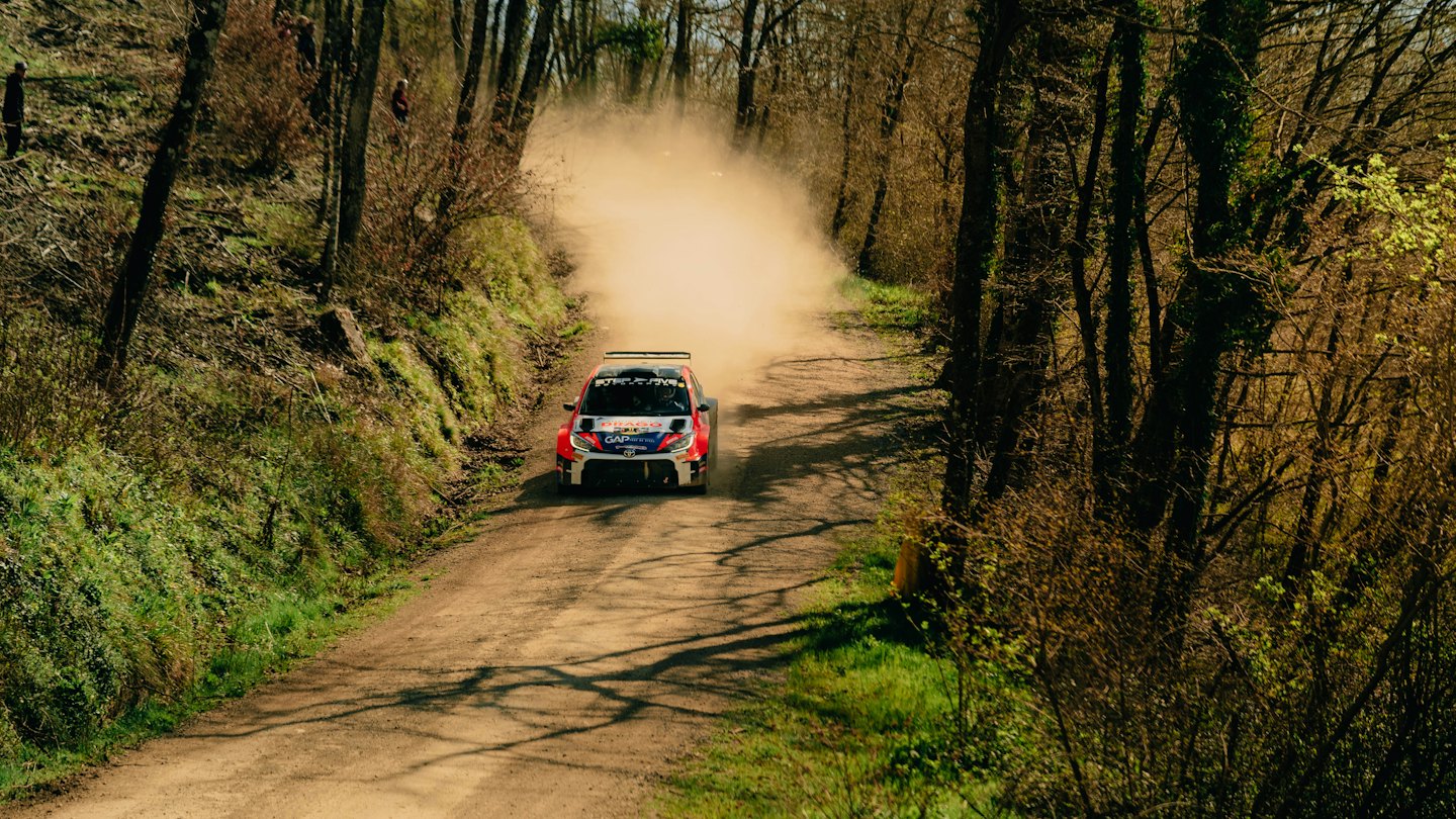 A red, white, and blue rally car speeds along a dusty track.