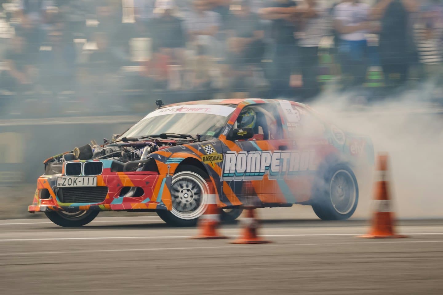 A drift car slides sideways on a track with tire smoke.