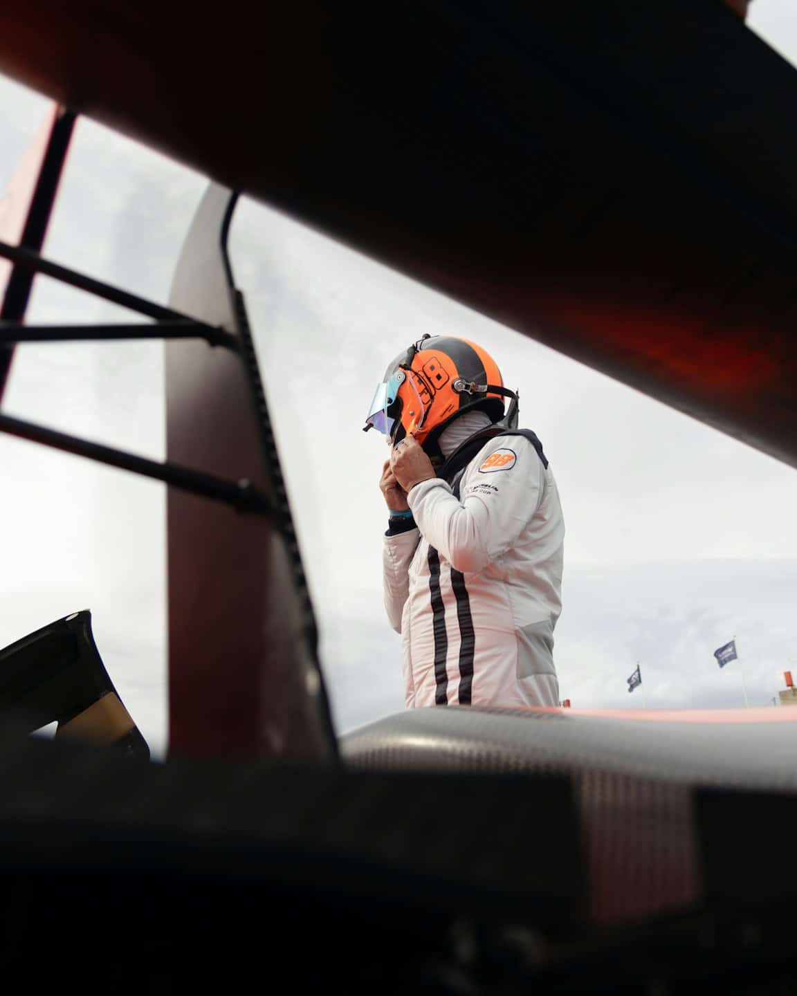 Race car driver in a racing suit adjusts their helmet.