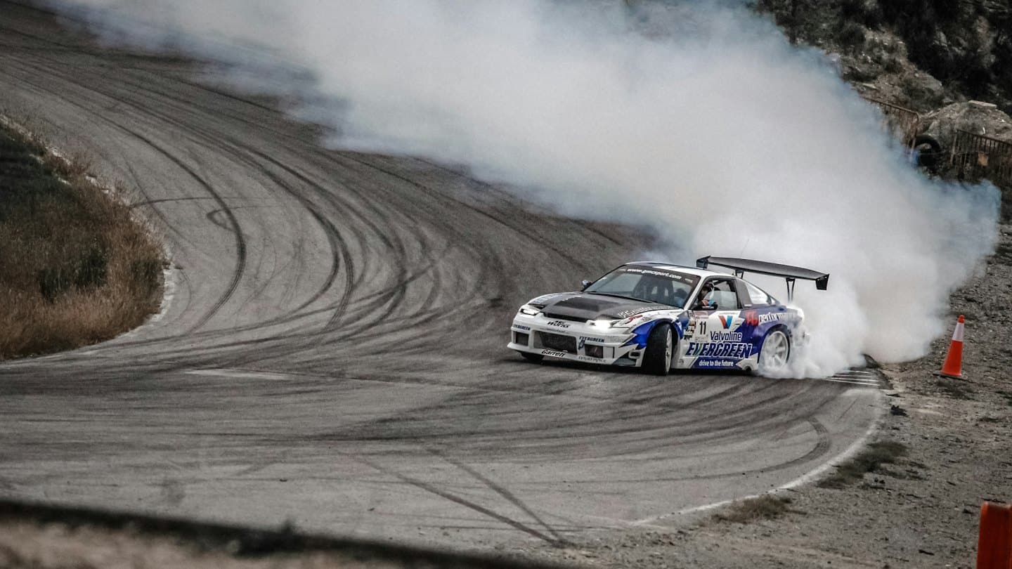 White and blue race car drifting on asphalt track with smoke.
