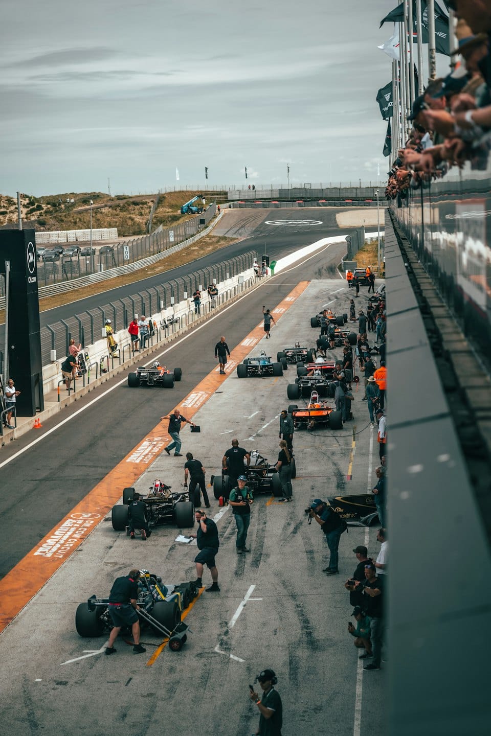Mechanics work on vintage race cars in a busy pit lane.
