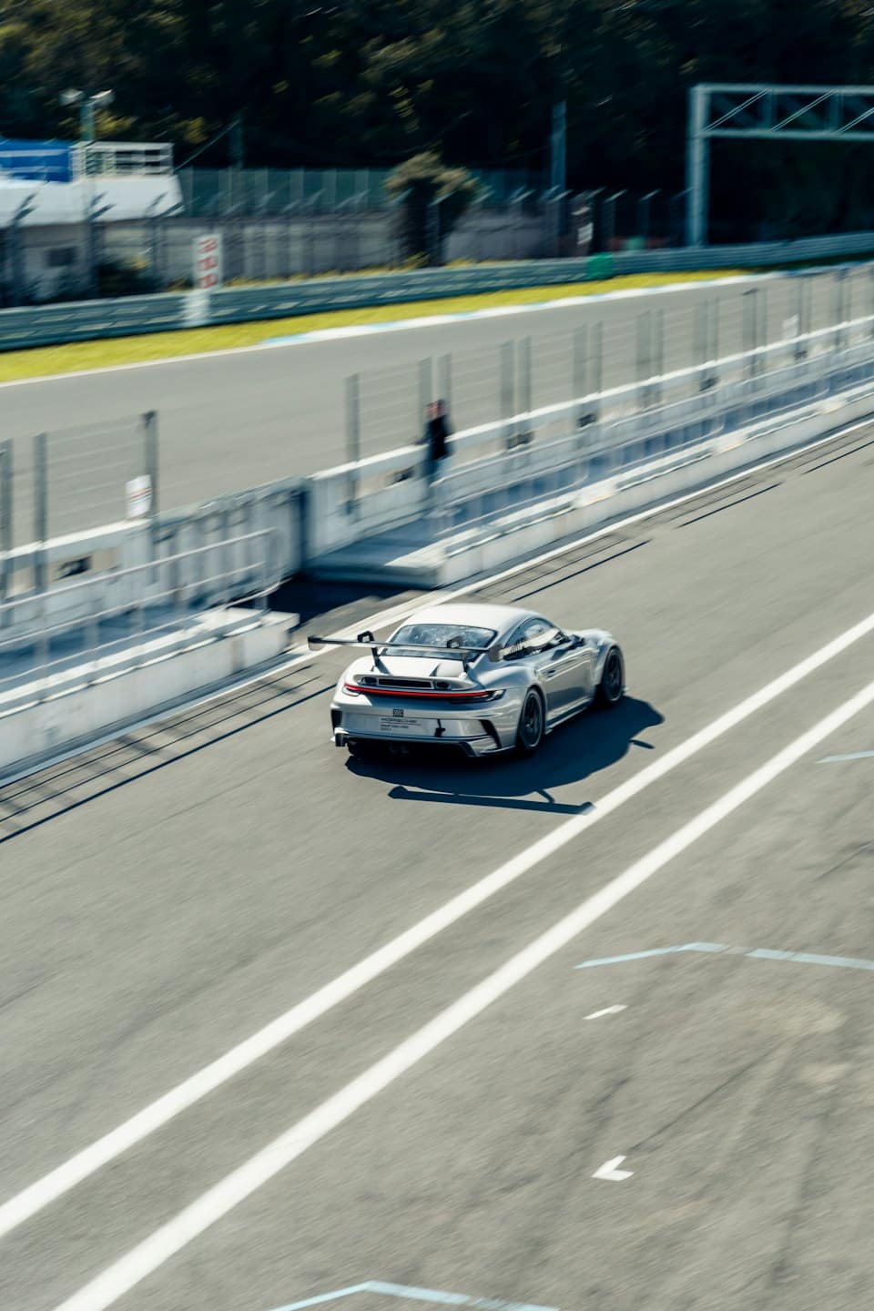 Silver sports car driving quickly on an asphalt racetrack.