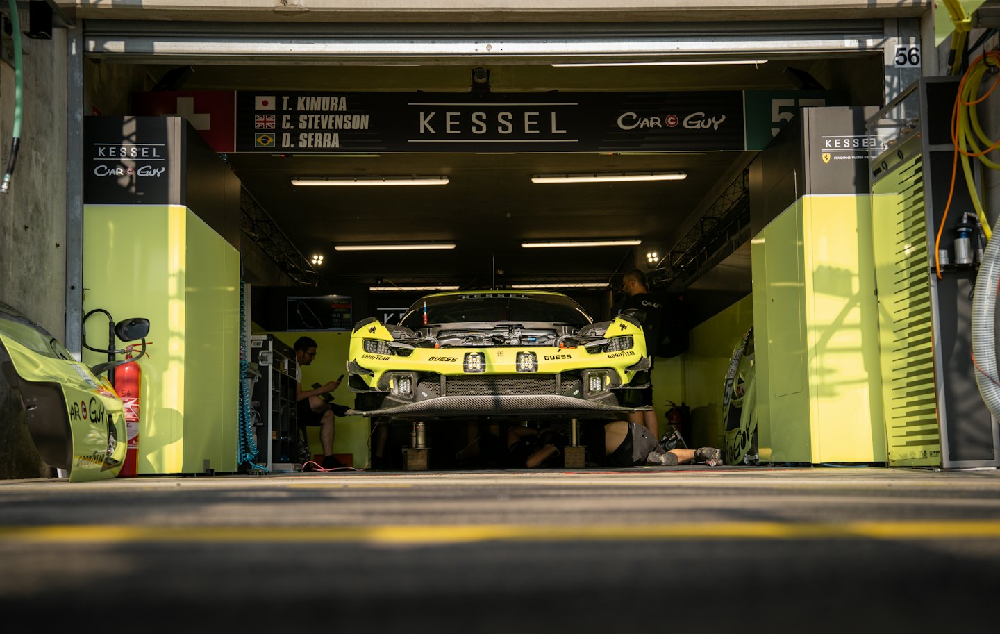 Mechanics work on a yellow sports car inside a garage.