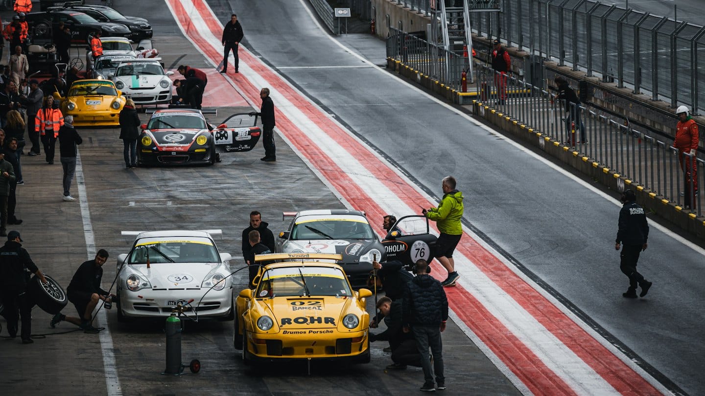 Mechanics work on race cars at a wet pit lane.