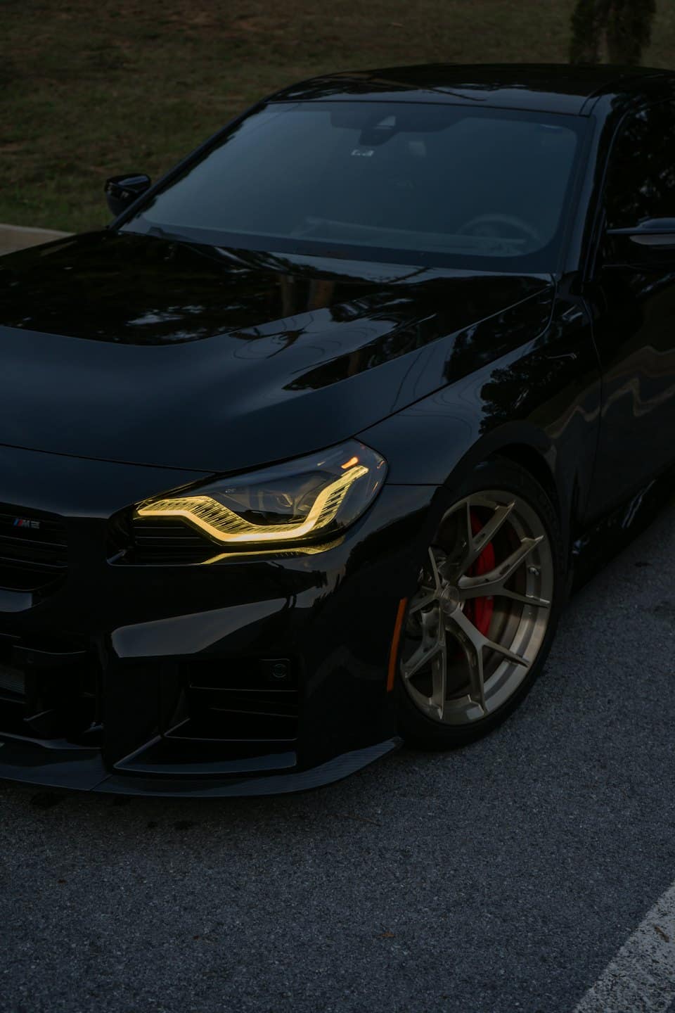 Sleek black sports car with glowing headlights and gold wheels parked at night.