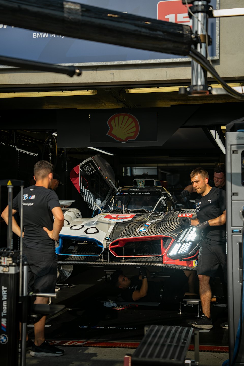 Three mechanics perform maintenance on a race car in a garage.